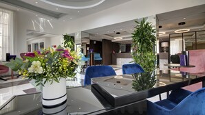 A modern lobby with a glass coffee table, blue chairs, and a large potted plant. - Urban Valley Resort (San Gwann)