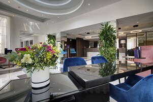 A modern lobby with a glass coffee table, blue chairs, and a large potted plant.