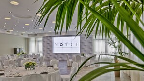 A conference room with round tables, white chairs, and a projection screen displaying "The Notch". - Urban Valley Resort (San Gwann)