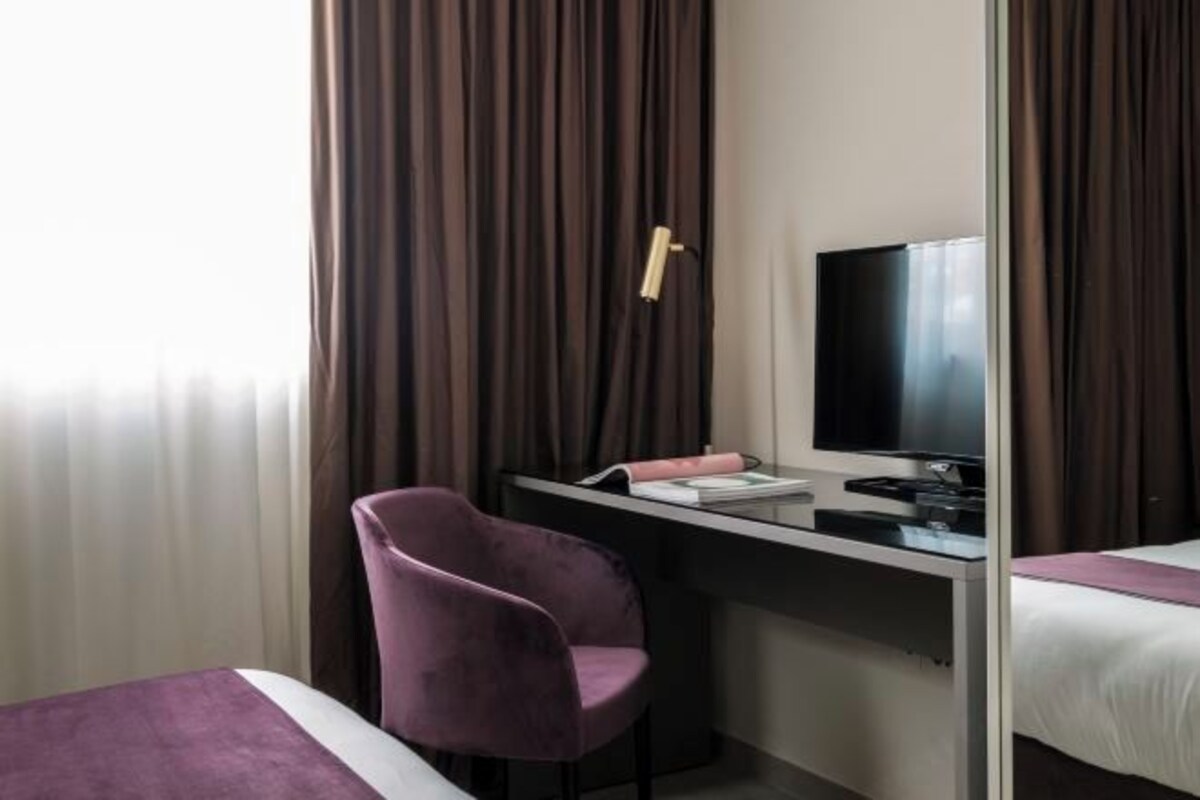 A hotel room with a bed, a desk with a TV, a chair, and curtains.