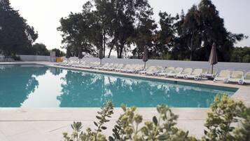 Piscina con lettini e ombrelloni bianchi, immersa nel verde.