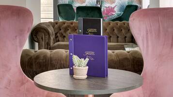 A room with a tufted brown sofa, a round table with a potted plant, and a vibrant tropical leaf wallpaper.