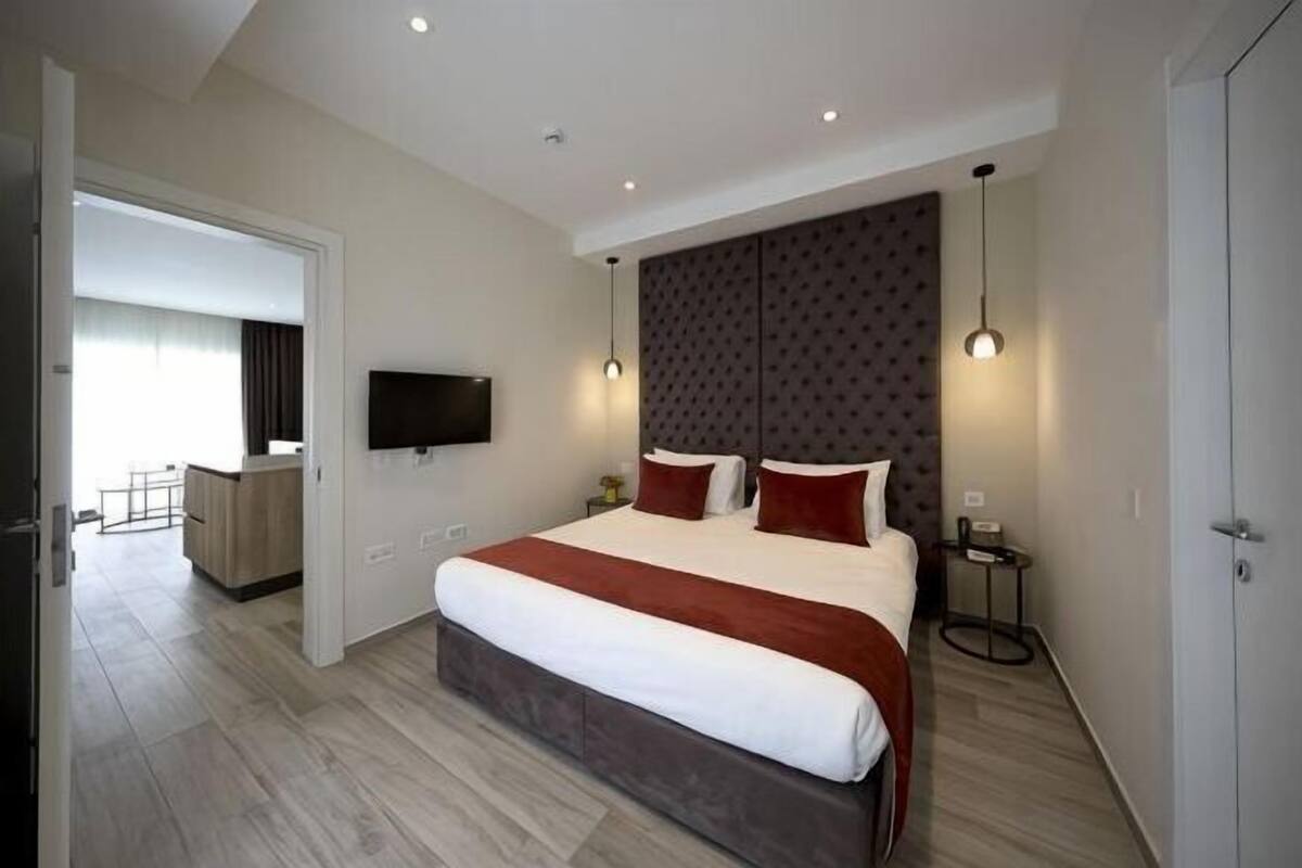 A modern hotel room with a large bed, a flat-screen TV, a bedside table, and a small desk area.