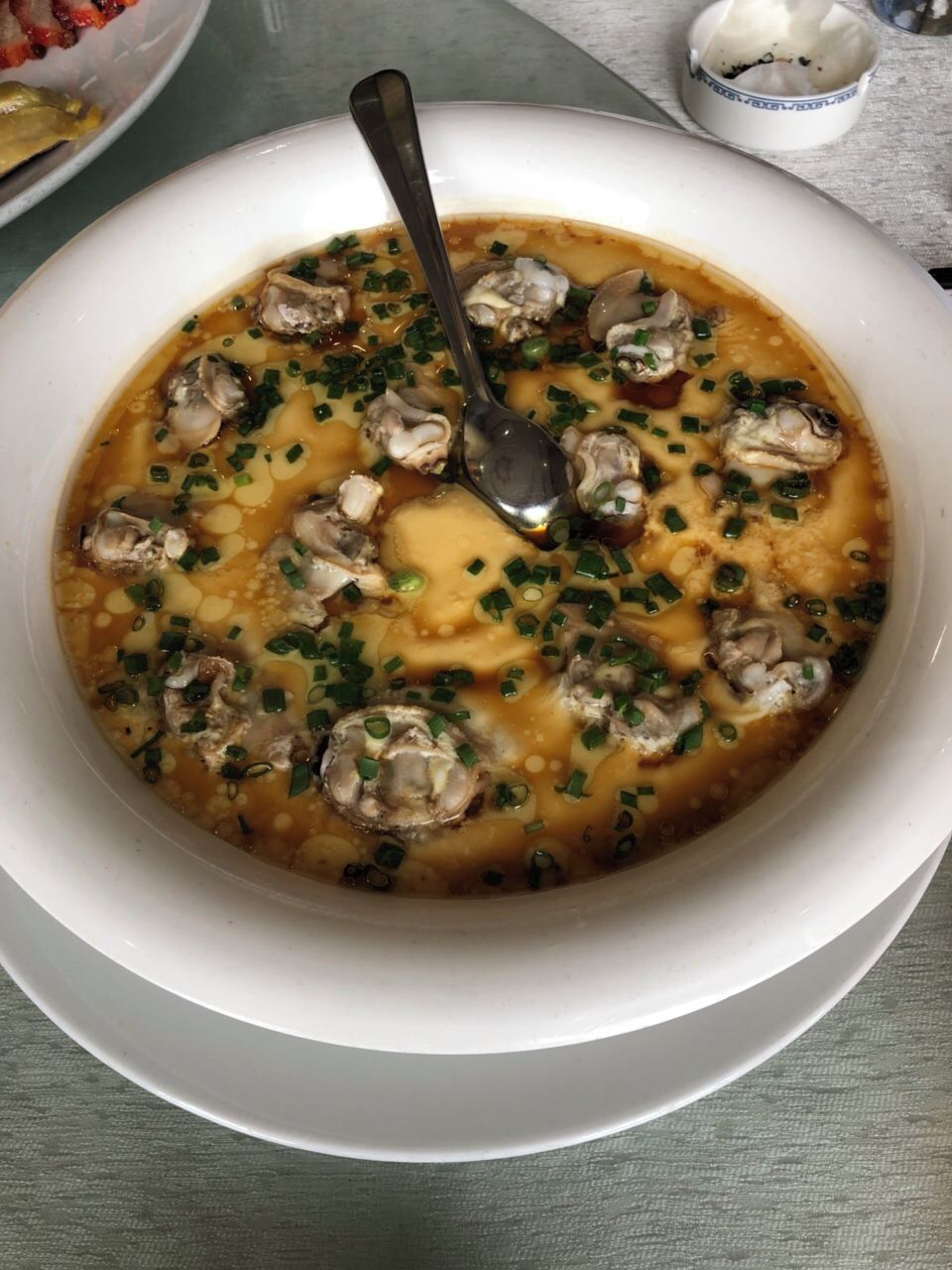A bowl of soup with mushrooms and green onions, accompanied by a spoon.