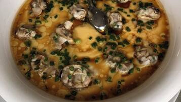 A bowl of soup with mushrooms and green onions, accompanied by a spoon.