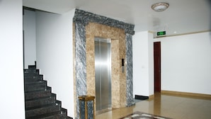 A lobby with a marble elevator, a wooden bench, and a patterned rug.