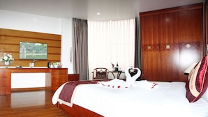 A hotel room with a wooden desk, a television, a bed with a swan-shaped pillow, and a large window with curtains.