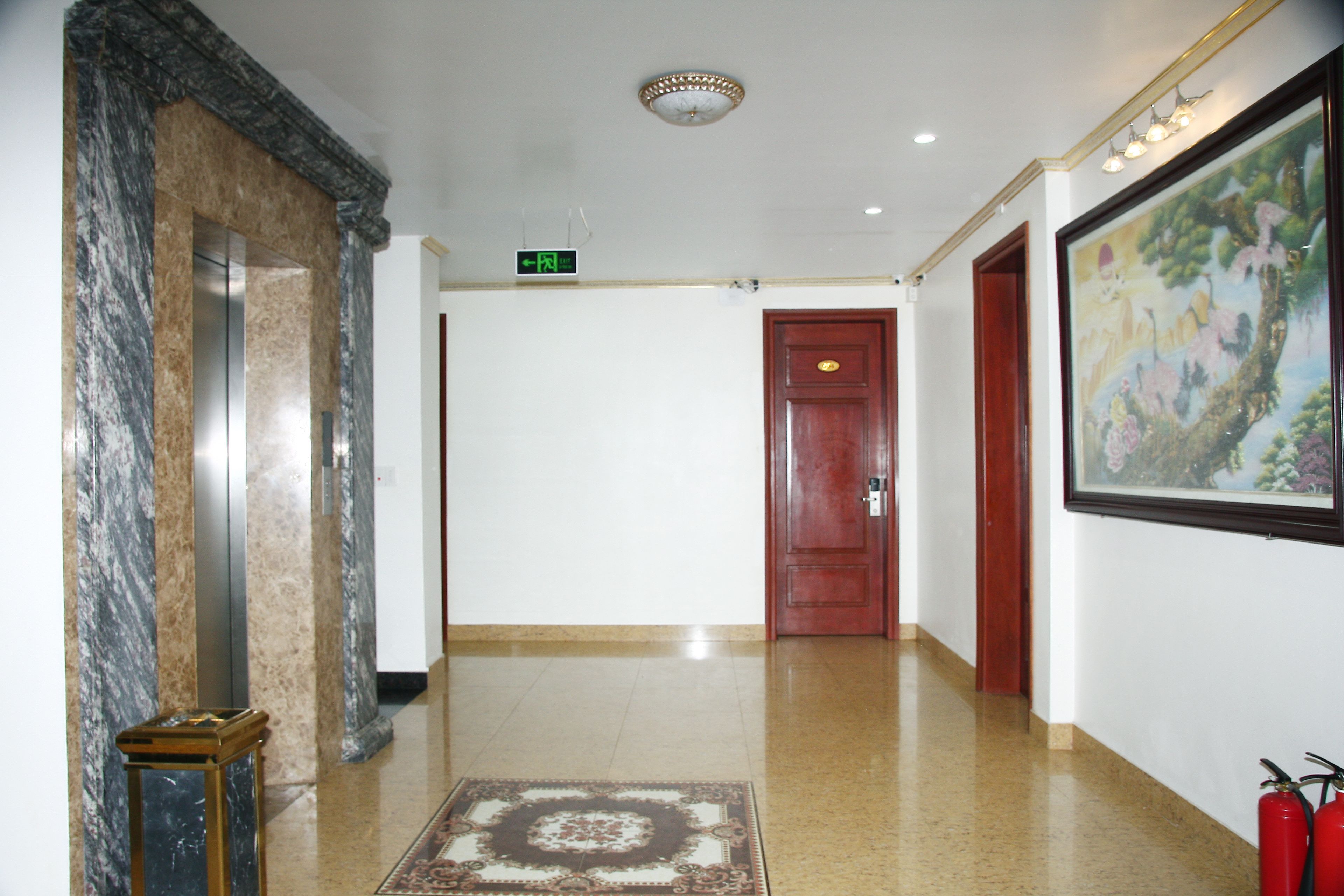 En hall med en marmorkolonn, en brandsläckare och ett inramat konstverk på väggen.