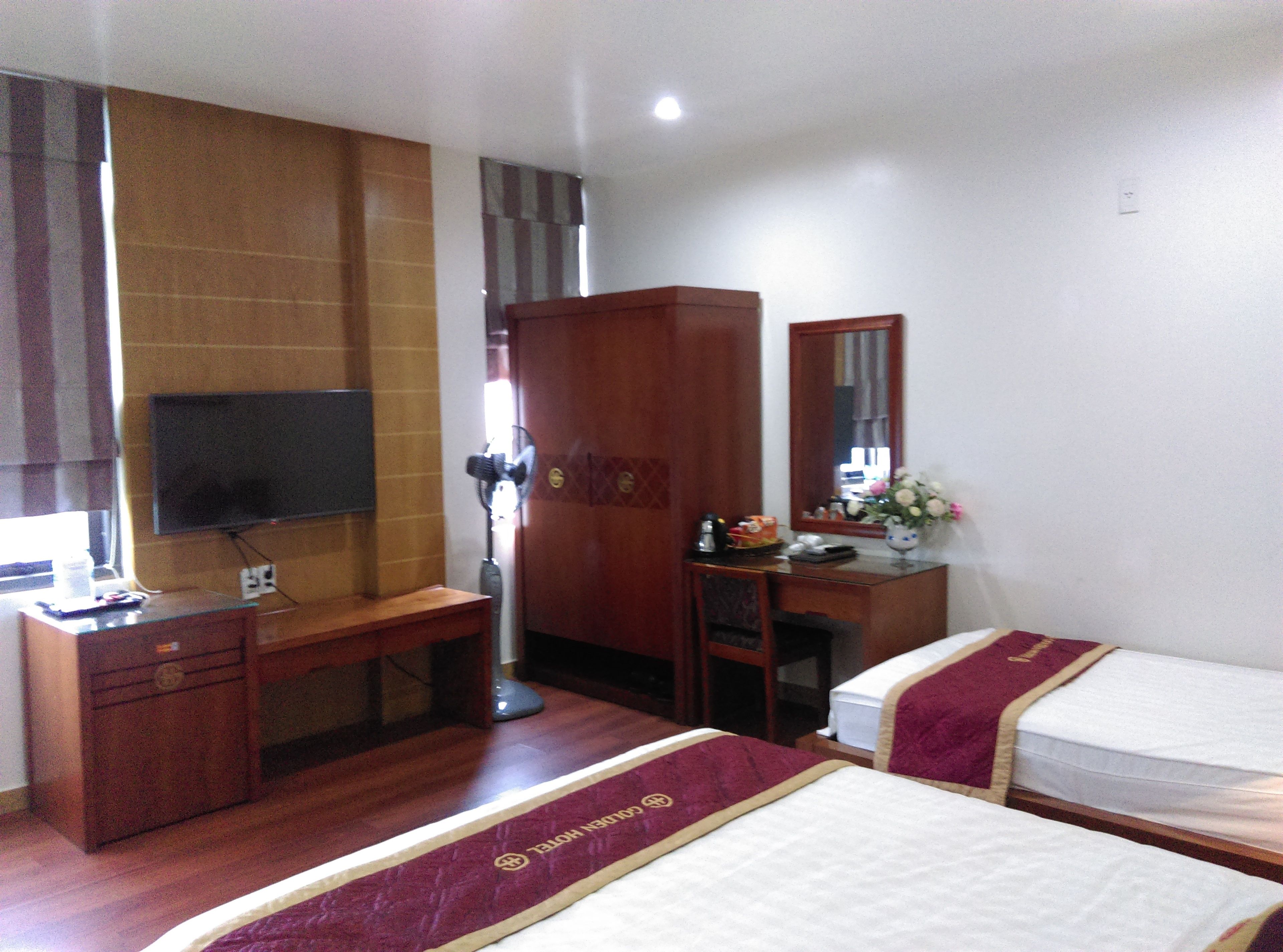 A hotel room with two beds, a desk with a television, a wardrobe, and a mirror.