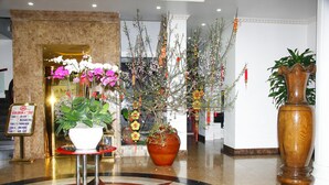A lobby with a marble floor, a reception desk, a large potted plant, and a signboard.