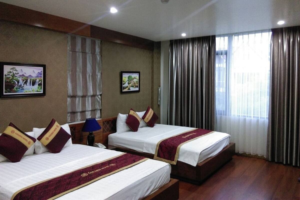 A hotel room with two beds, a nightstand, a lamp, and curtains.