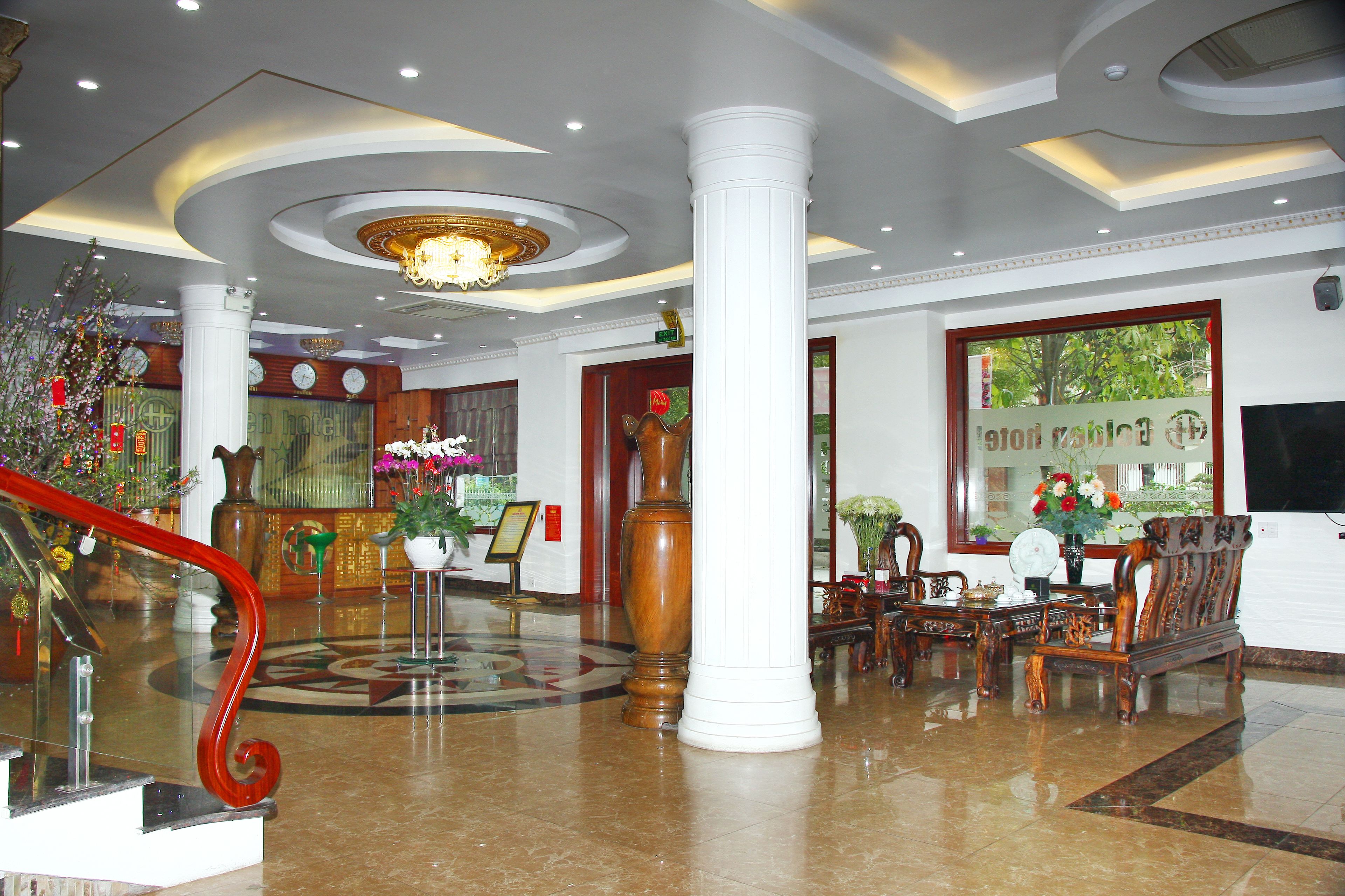 A lobby with a grand staircase, a chandelier, a reception desk, and a seating area with a large window.