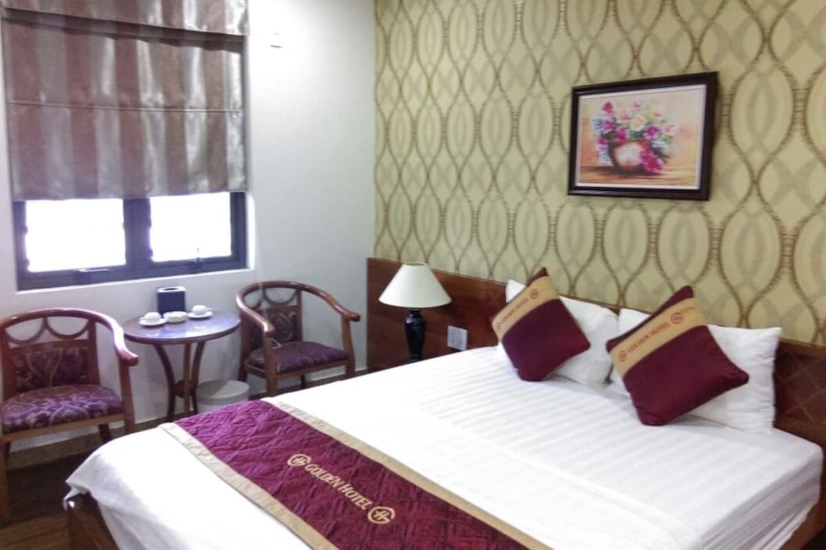 A hotel room with a bed, two chairs, a small table, a lamp, and a window with curtains.