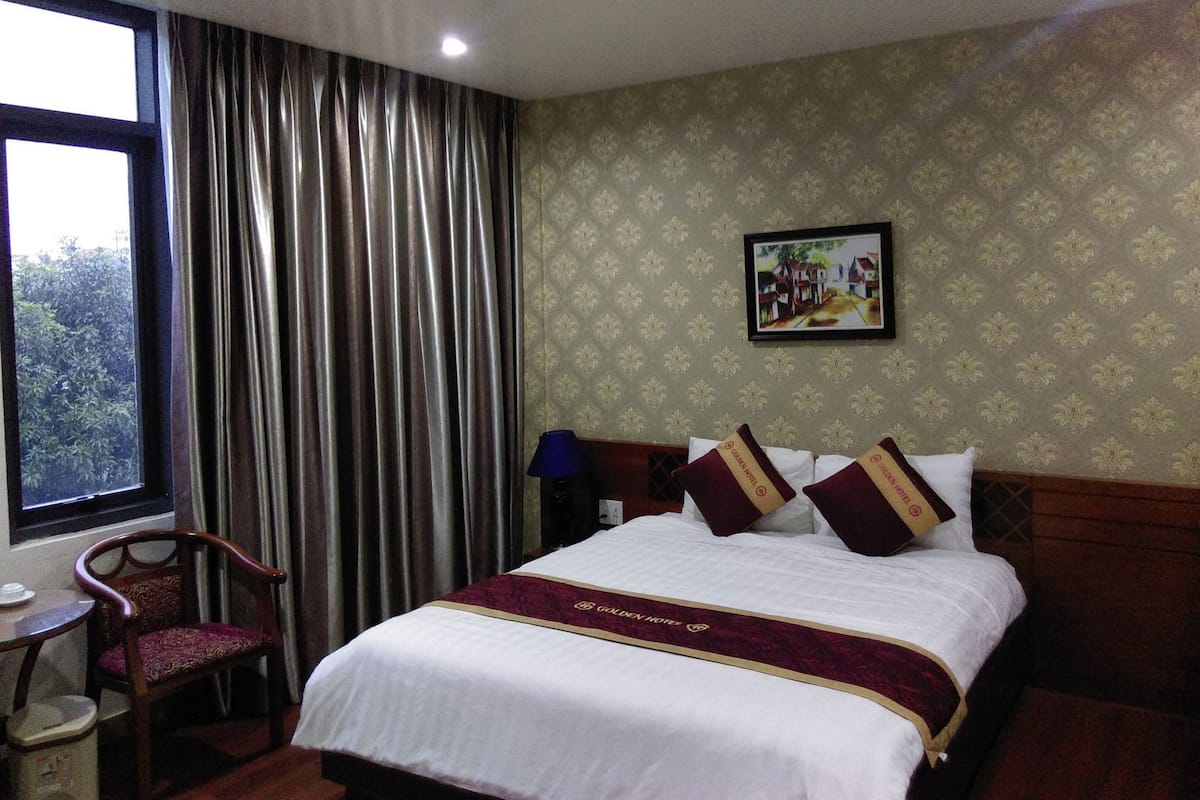 A hotel room with a bed, a chair, a table, and a window with curtains.