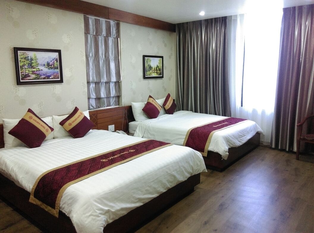 A hotel room with two beds, each with white bedding and maroon pillows, a wooden headboard, and a large window with curtains.