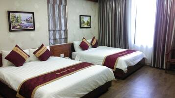 A hotel room with two beds, each with white bedding and maroon pillows, a wooden headboard, and a large window with curtains.