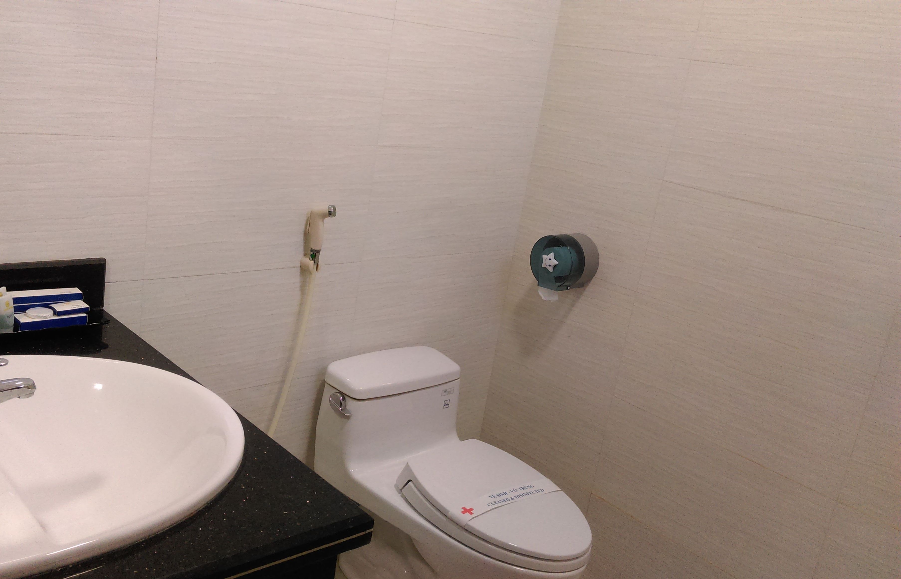 Une salle de bain avec un lavabo blanc, des toilettes et un sèche-mains fixé au mur.