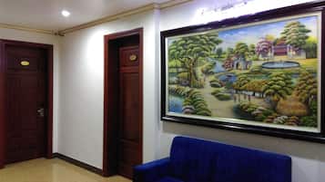 A lobby with a blue sofa, a framed painting of a landscape, and two wooden doors.