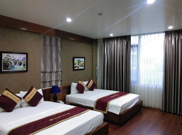 A hotel room with two beds, each with a red and gold headboard, a nightstand with a lamp, and a large window with curtains. - Golden Thai Binh Hotel (Thai Binh)
