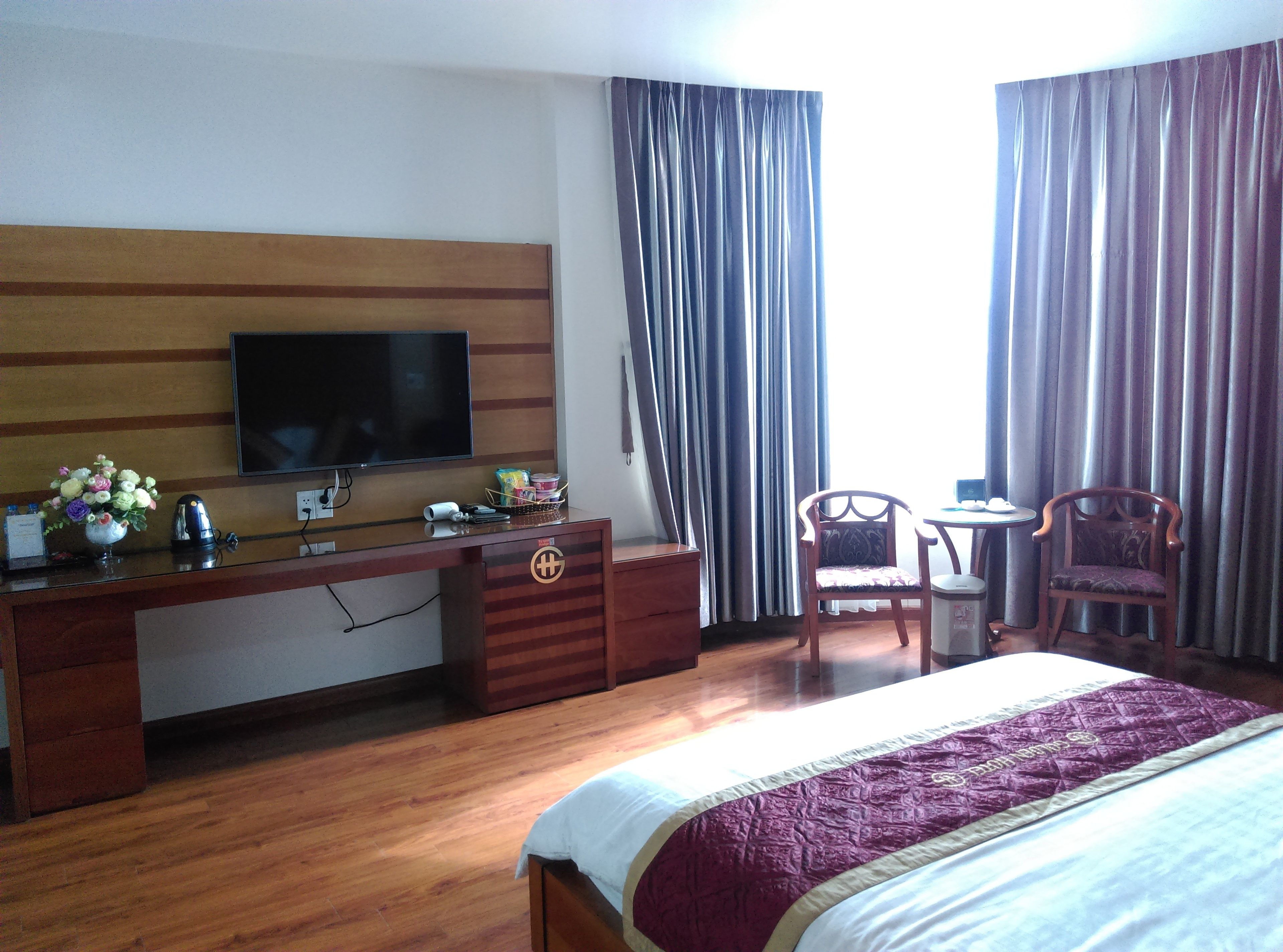Une chambre d’hôtel avec un lit, un bureau avec une télévision, une chaise et une fenêtre avec des rideaux.