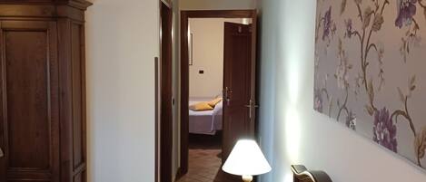 Un dormitorio con una cama, un armario de madera, una lámpara sobre una mesita de noche y un papel pintado con motivos florales.