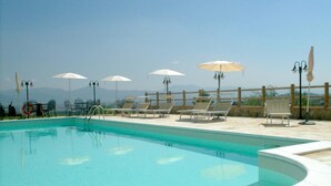 Una piscina con agua cristalina azul, rodeada de sillas de descanso y sombrillas, con vistas a montañas al fondo.