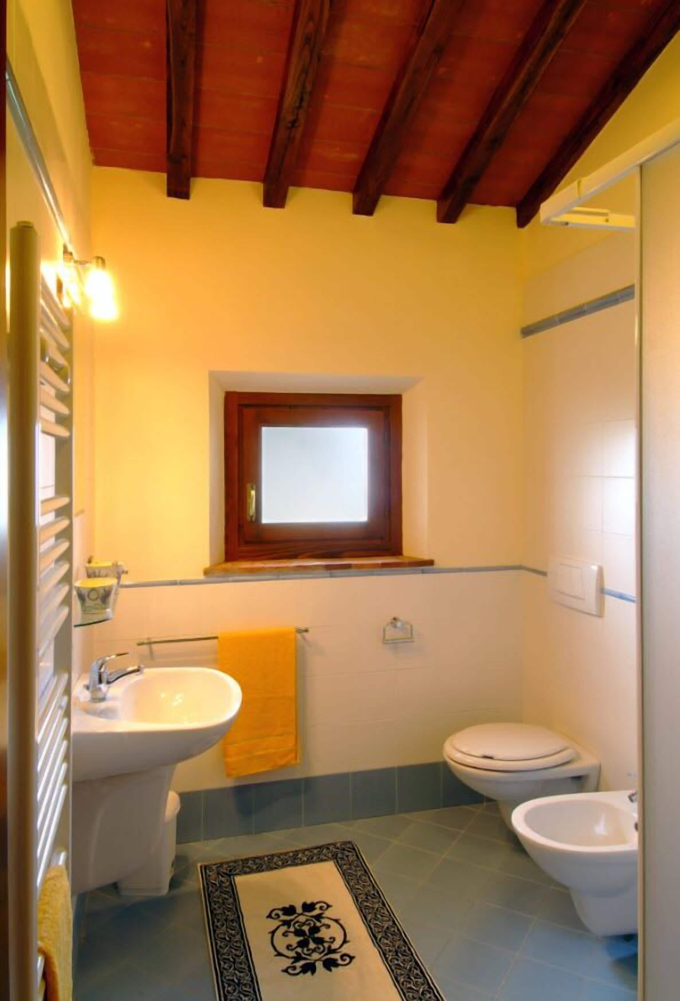A bathroom with a sink, toilet, bidet, and a small window.