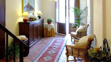 A spacious living area with a wooden staircase, a dining table with chairs, a patterned rug, and a large window providing natural light.