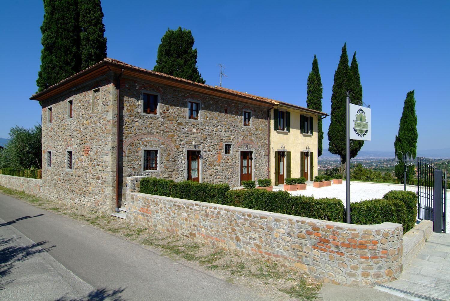 A stone building with a red-tiled roof, a stone wall, and a sign indicating it is a hotel.