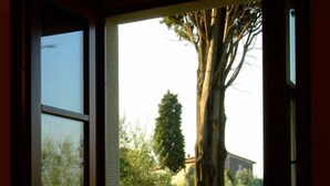 Puerta abierta que da a un jardín con mobiliario de mimbre y un gran árbol.