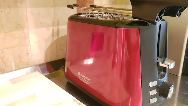 Ein rotes Toastermodell mit schwarzem Bügel und digitaler Anzeige auf einer Küchenarbeitsplatte.