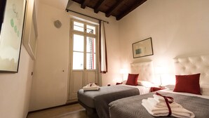A hotel room with two beds, a large window with curtains, a framed picture on the wall, and a wooden ceiling. - Bright Apartments Verona - Borsari Historical 1 (Verona)