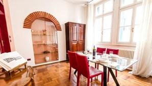 A dining area with a glass table, red chairs, a wooden cabinet, and a window with curtains. - Bright Apartments Verona - Borsari Historical 1 (Verona)