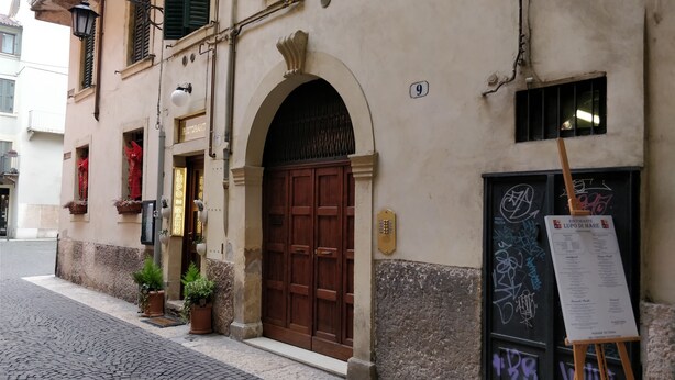 A building with a large wooden door, a sign reading "LUPO DI MARE," and a menu board on the right. - Bright Apartments Verona - Borsari Historical 1 (Verona)
