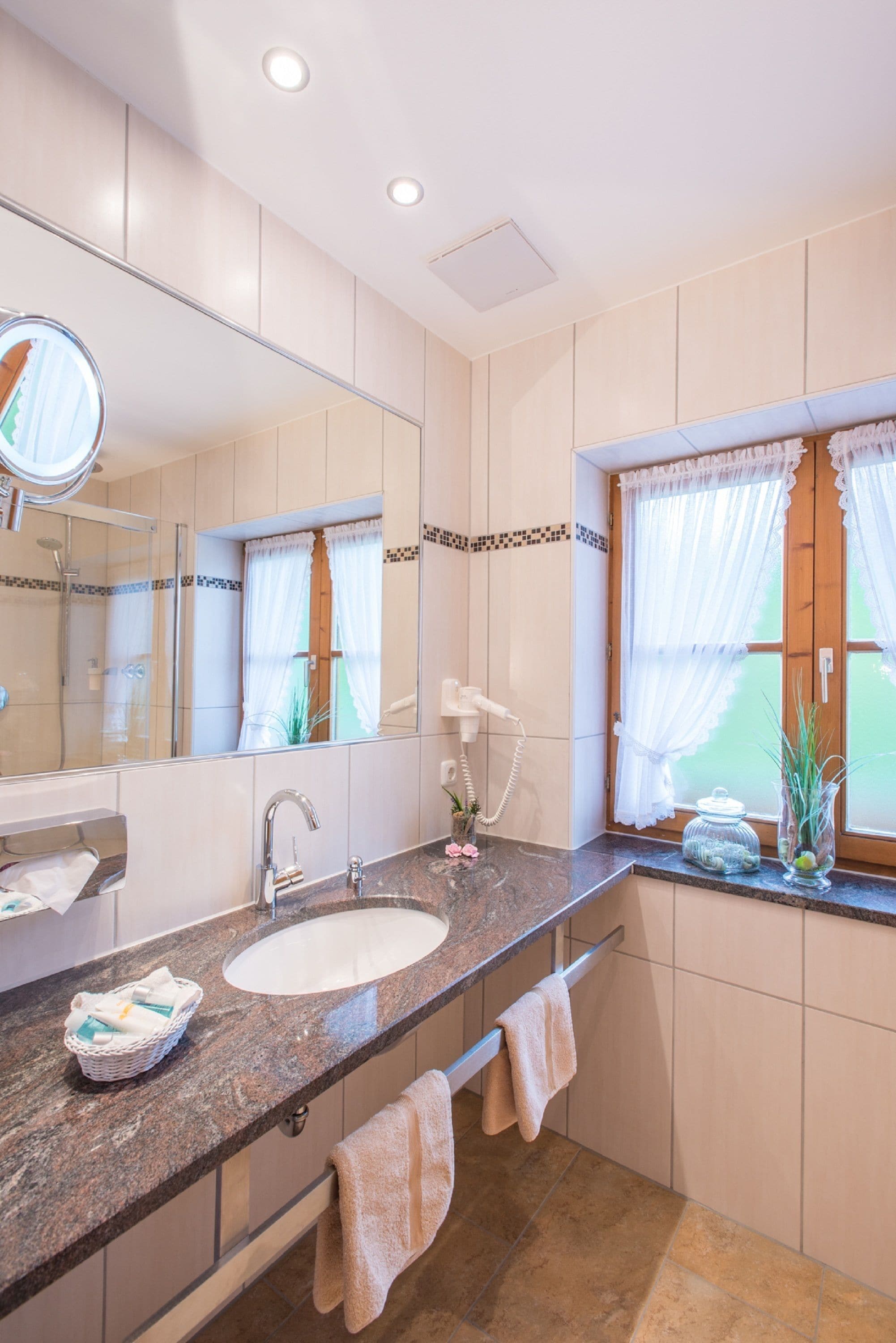 Un baño con un espejo grande, un lavamanos y un ventanal con cortinas.