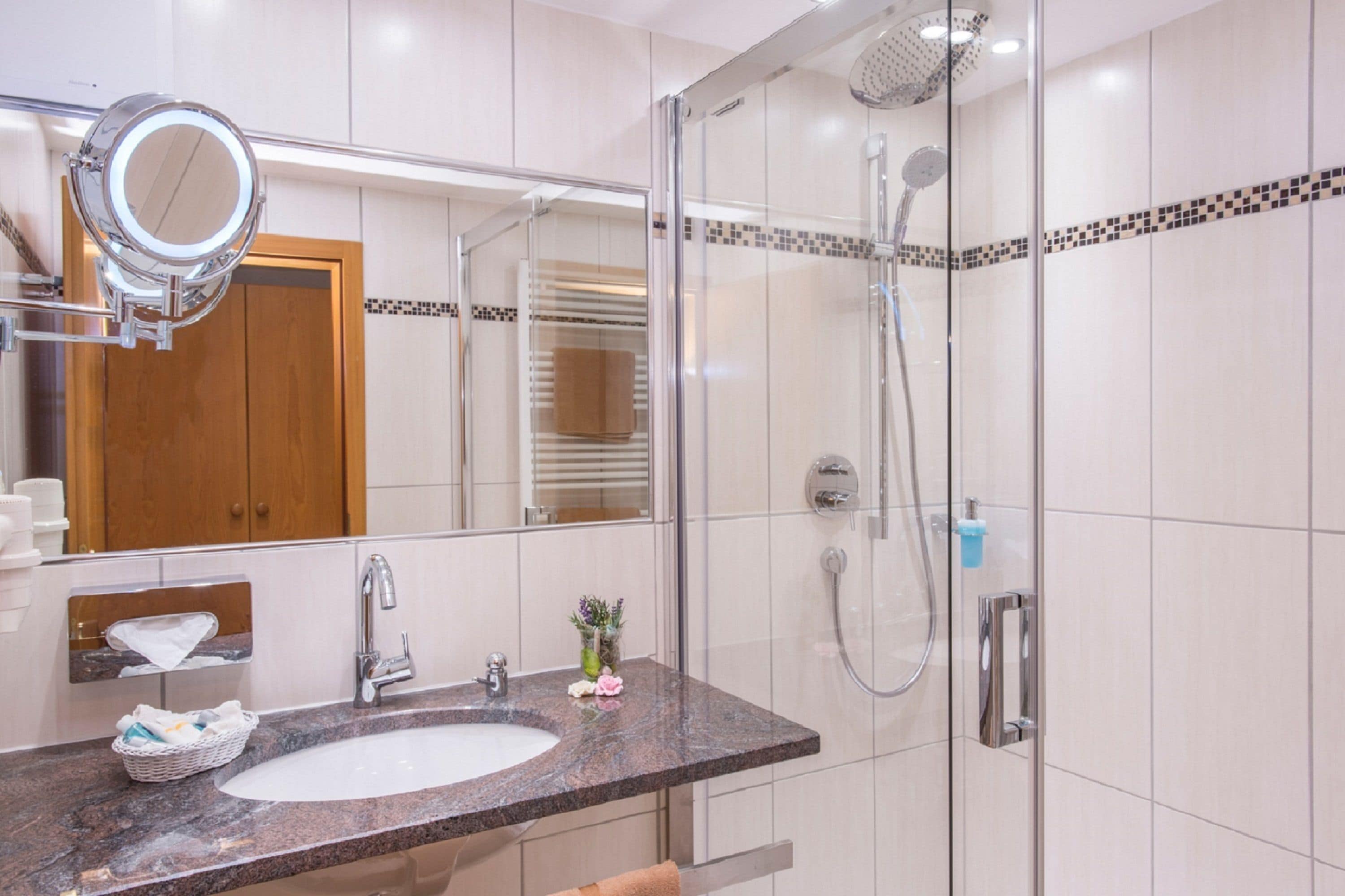 Une salle de bain moderne avec un lavabo surmonté d’un plan de travail en granit, une douche à parois de verre et une porte en bois à l’arrière-plan.
