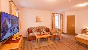 Una sala de estar con televisor, sofá, sillón, una mesa con frutas y una puerta de madera.
