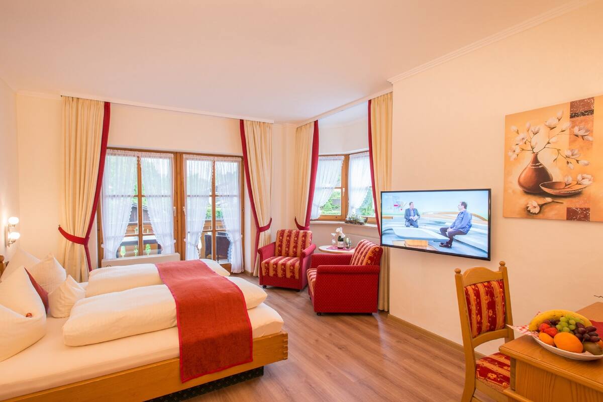A hotel room with a bed, two red chairs, a television, and a fruit bowl.