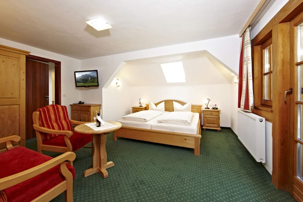 A hotel room with a bed, a chair, a small table, a television, and a window.
