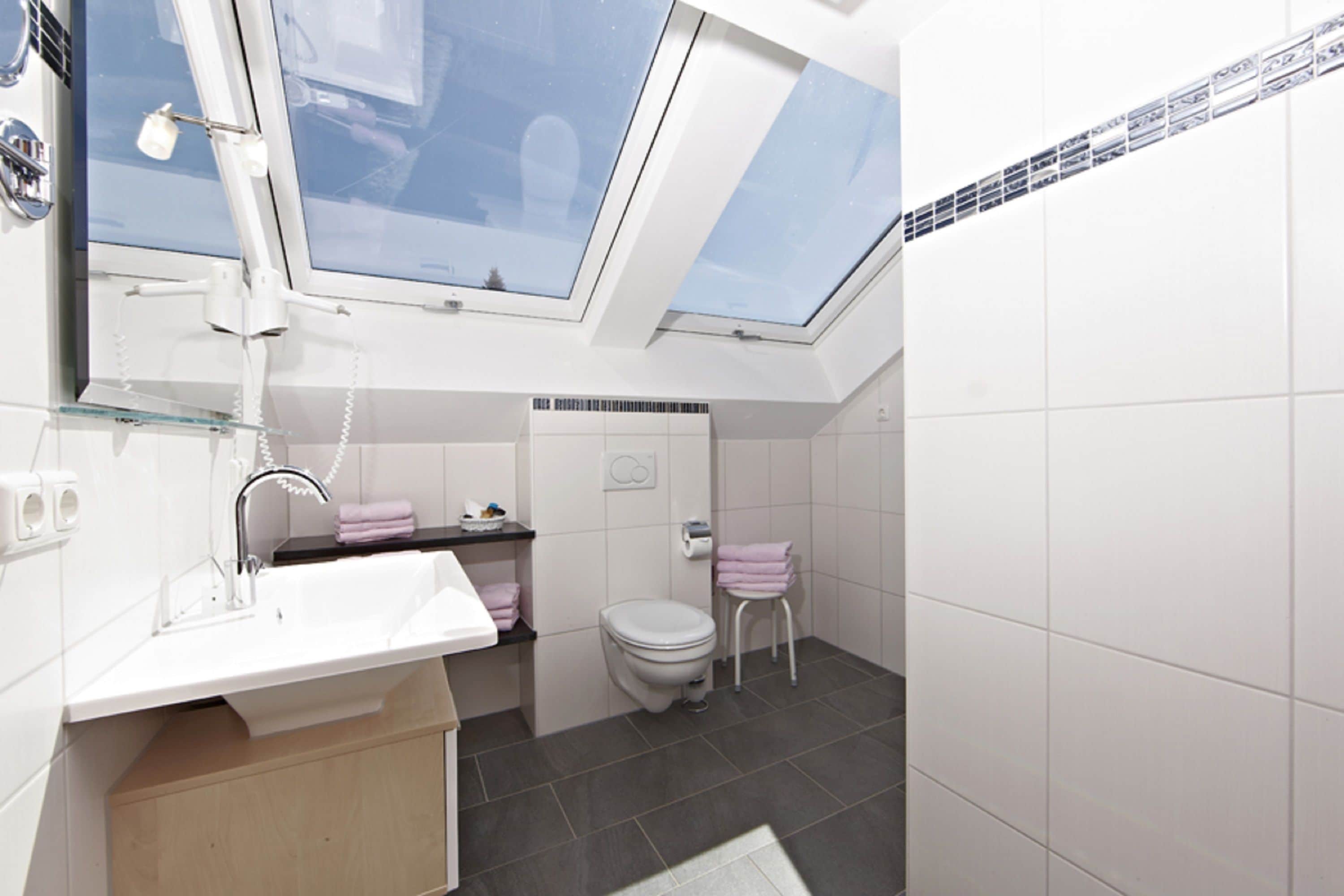A modern bathroom with a skylight, a white sink, a toilet, and a small stool.