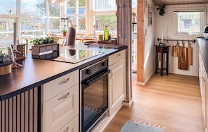 A modern kitchen with a large island, white cabinetry, and a view of the outdoors through large windows.