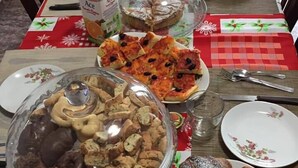 Una mesa de comedor dispuesta con diversas comidas, entre ellas pizza, pasteles y un recipiente cubierto con galletas.