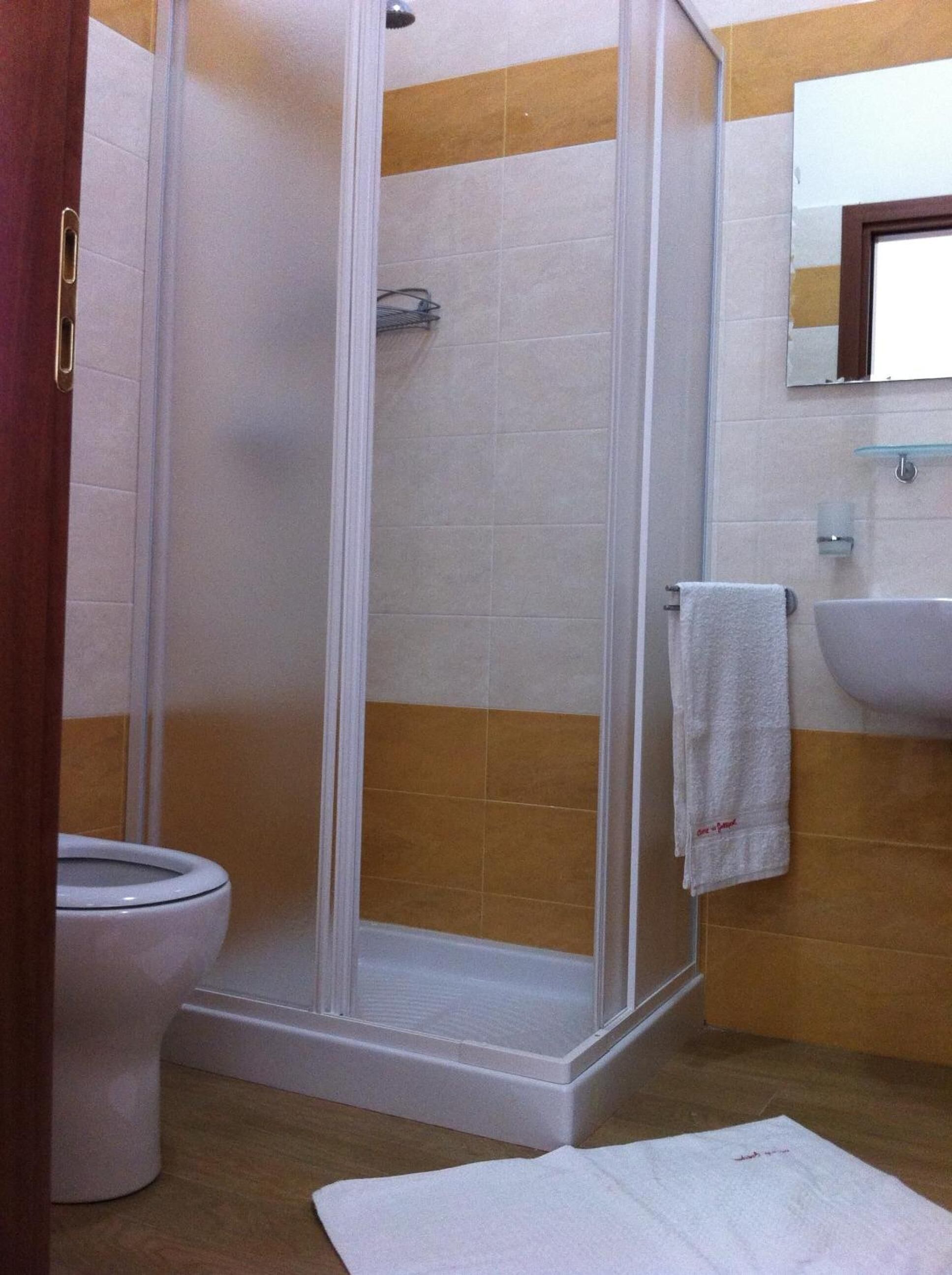Un baño con cabina de ducha de vidrio, inodoro blanco y lavamanos con espejo.