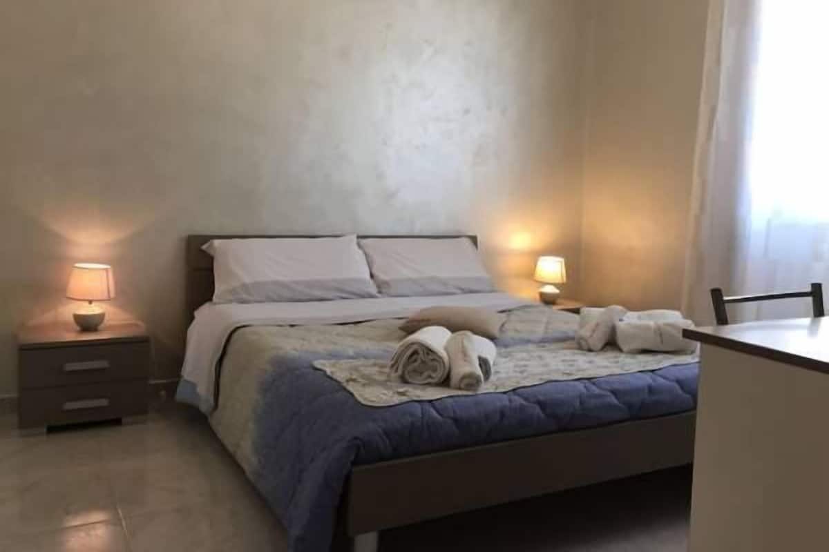 Een slaapkamer met een bed, nachtkastjes en een stoel.