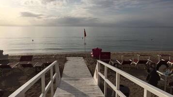 Una passera de fusta que condueix a una platja, amb files de gandules buides i una bandera vermella a la sorra.
