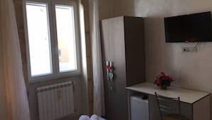 Una habitación con cama, escritorio, silla, televisor y ventana.