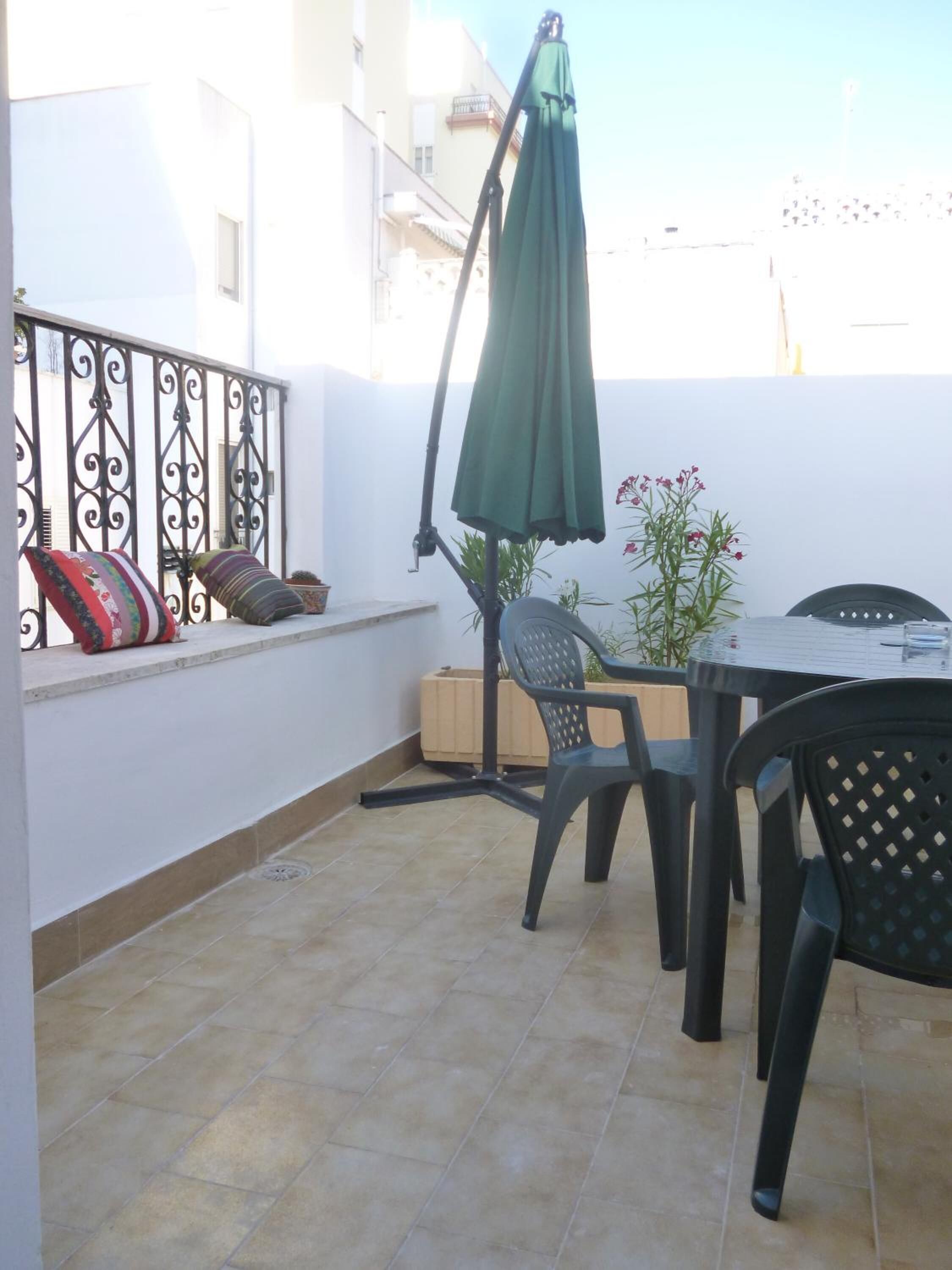 A balcony with a table and chairs, a green umbrella, and a potted plant.