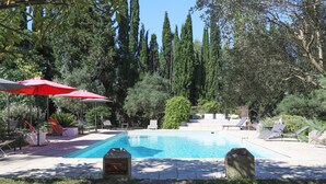 A swimming pool with red umbrellas, lounge chairs, and a stone monument. - Chateau d'Agel (Agel)