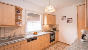 A modern kitchen with wooden cabinets, a granite countertop, a built-in oven, and a coffee maker. - Komfort-Ferienhaus Alpspitz (Grainau)