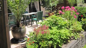 A wooden house with a balcony, surrounded by lush greenery and flowering plants. - Komfort-Ferienhaus Alpspitz (Grainau)